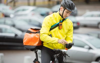Young male cyclist with courier delivery bag using mobile phone on street