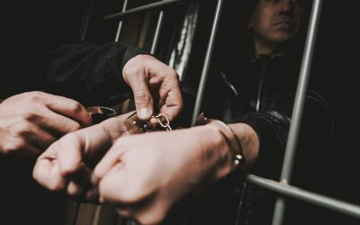 A Man In Handcuffs Is Behind Bars In A Police Station. Jailed Suspect. Bandit In Leather Jacket. Successful Arrest. Commit A Crime. Guilt Negation. Close-up Criminal. Citizen's Protection.